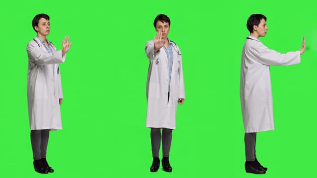 Woman physician raising palm and doing stop sign in studio, expressing rejection and denial against greenscreen backdrop. General practitioner showing warning symbol with negative reaction. Camera A.