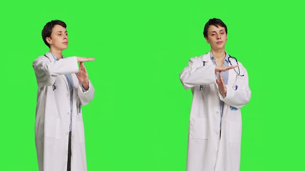 Woman physician doing timeout gesture against greenscreen backdrop, asking for a work break after multiple examinations. Doctor showing pause or stop symbol, feeling tired. Camera B.