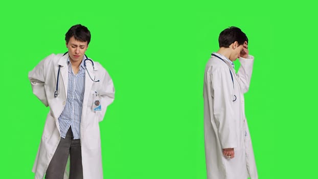 Medic in white coat suffering from migraine and lower back pain, feeling overworked and stressed at hospital. Unwell doctor with headache and spine discomfort against greenscreen backdrop. Camera B.