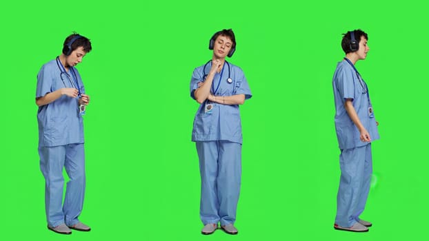 Cheerful health specialist listening to cool music on audio headset, dancing against greenscreen backdrop and having fun. Nurse enjoying songs an doing funny dance moves, leisure. Camera A.