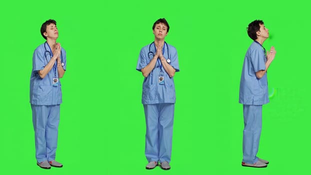 Medical assistant being hopeful praying for good luck against greenscreen, holds hands in a prayer sign and having belief in spirituality. Young christian nurse with faith in meditation. Camera A.