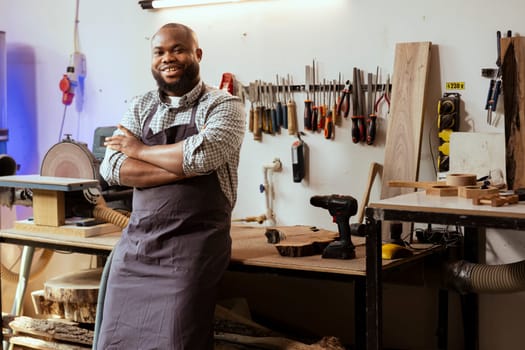 Portrait of smiling african american carpenter preparing to start production in messy furniture assembly shop. Happy BIPOC manufacturer at workbench ready to cut wood pieces