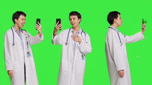 Medic specialist having remote videocall conversation with patients on smartphone internet connection, greenscreen backdrop. Doctor discusses about disease with people on videoconference. Camera B.