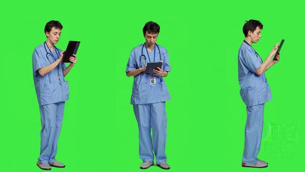 Medical assistant browsing online webpages on tablet and texting, using social media apps to chat with people. Nurse navigates internet on gadget, standing against greenscreen backdrop. Camera A.
