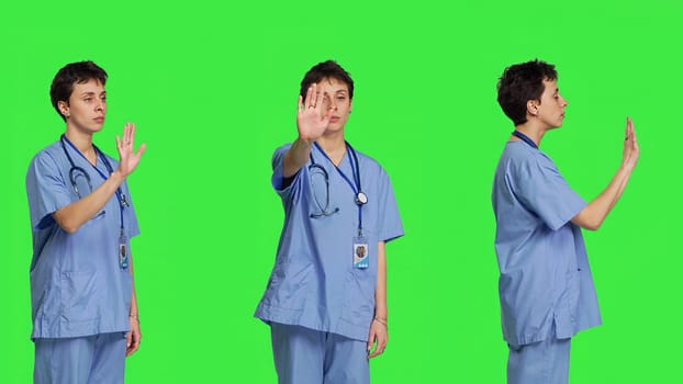 Health specialist with blue scrubs showing stop sign in studio, standing against greenscreen backdrop. Nurse expressing denial and refusal with warning forbidden symbol, denying something. Camera B.