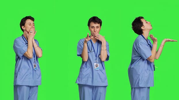 Flirty cute nurse blowing air kisses against greenscreen backdrop, being romantic and expressing sweet feelings. Medical assistant in scrubs doing lovely gesture, expressing true love. Camera B.