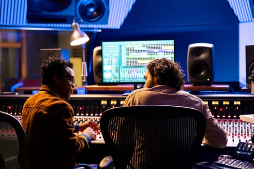 Team of sound technician and singer working on new music, mixing tunes on digital software in control room. Musician and producer collaborating on a new album, mixing and mastering tracks.