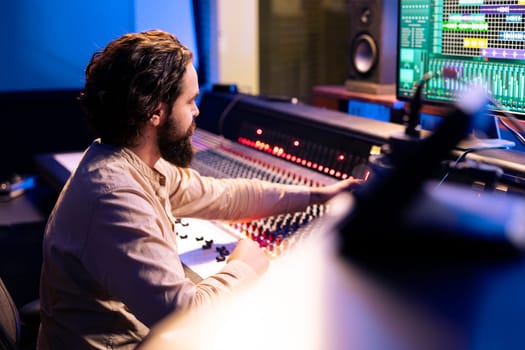 Music producer working on a new album in control room at studio, recording and processing sounds before editing in post production. Audio technician using daw software and mixing console.