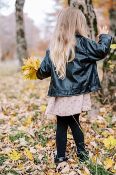 Little girl with a bouquet of yellow leaves stands in an autumn park, looking at her feet. High quality photo