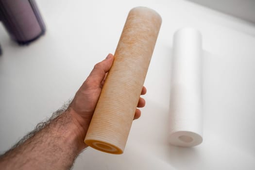 Man holding replaced dirty filter in reverse osmosis filter, while new lying on the table.