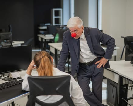 Elderly Caucasian man wearing a clown nose swears at his subordinate in the office