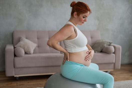 Caucasian pregnant woman suffers from belly pain. Fitball training during pregnancy
