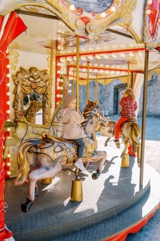 Little girls ride a toy horses on a colorful carousel. Back view . High quality photo