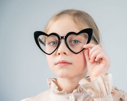 Portrait of a cute little girl wearing heart-shaped glasses on a white background