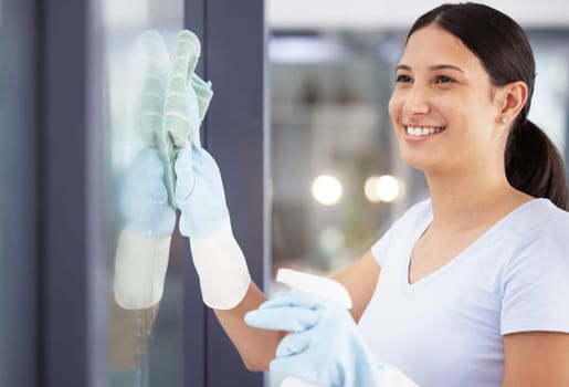 Happy woman, cleaner and wiping window with spray bottle for disinfection, hygiene or health and safety at office. Female person or young maid with smile for clear glass, surface or domestic service.