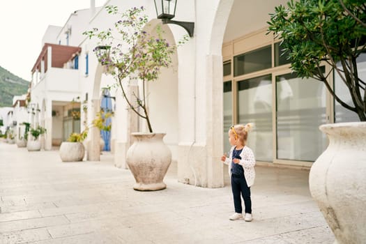 Little girl stands near an apartment building and looks away. High quality photo