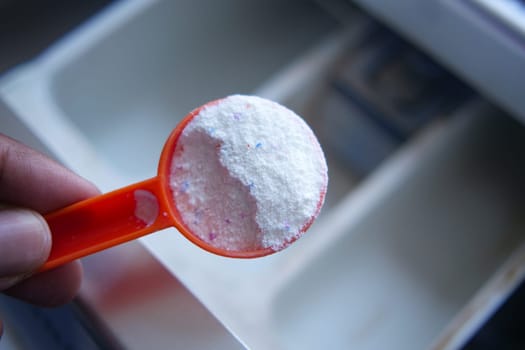 Washing powder in plastic spoon on black background top view