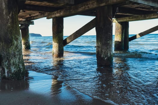 Storm sea waves under wooden pier in dramatic background wallpaper design. Seascape with running splashing sea waves. Sandy beach vacation getaway in Gdansk Poland. Copy space for your text