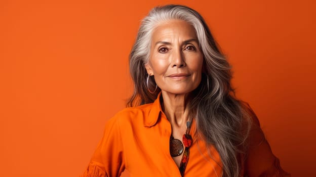 Elegant, elderly, chic Latino, Spain woman with gray long hair and perfect skin, orange background, banner. Advertising of cosmetic products, spa treatments, shampoos and hair care products, dentistry and medicine, perfumes and cosmetology for women
