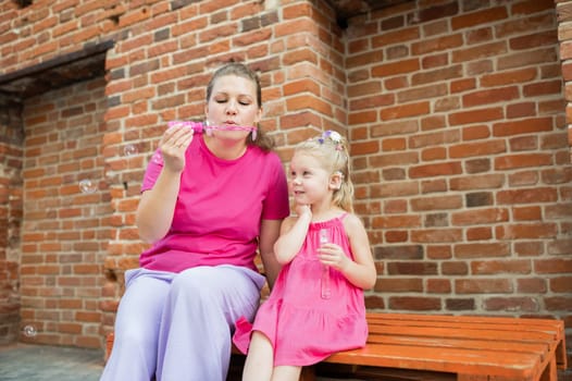 Deaf child with cochlear implant for hearing audio and aid for impairment having fun and laughs with mother outdoor in summer. Sound fitting device to help with communication listening and interaction.