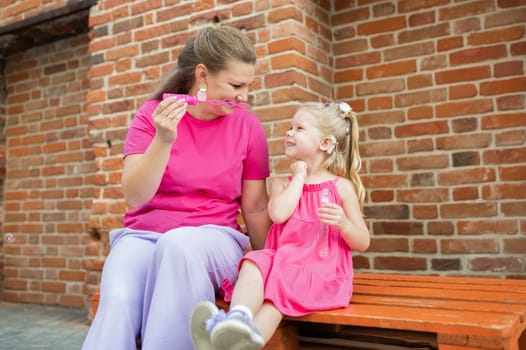 Blonde little girl with cochlear implant playing with her mother outdoor. Hear impairment deaf and health concept. Diversity and inclusion. Copy space.