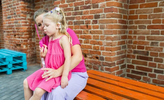 Blonde little girl with cochlear implant playing with her mother outdoor. Hear impairment deaf and health concept. Diversity and inclusion. Copy space.