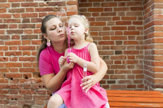 Deaf child with cochlear implant for hearing audio and aid for impairment having fun and laughs with mother outdoor in summer. Sound fitting device to help with communication listening and interaction.