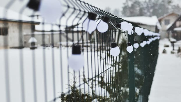 A white garland of bulbs on a fence in winter