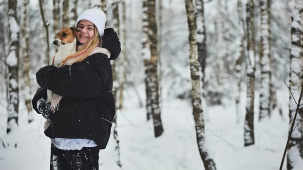 A girl cuddles a Jack Russell Terrier dog in the woods in winter