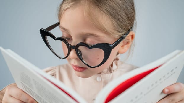 Portrait of a little girl in heart-shaped glasses reading a book