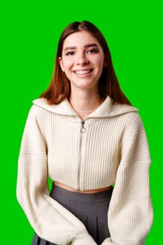 A cheerful young woman stands in front of a vivid green backdrop, wearing a cozy beige hoodie and grey leggings. Her hands are gently resting on her waist, and she sports a friendly, approachable smile. Her dark hair frames her face as she looks directly at the viewer.