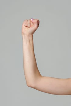 Female hand with clenched fist on gray background in studio