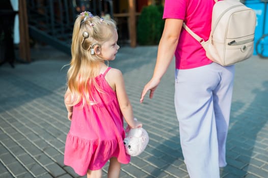 Blonde little girl with cochlear implant playing with her mother outdoor. Hear impairment deaf and health concept. Diversity and inclusion. Copy space.