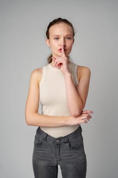 Young Woman Making a Hush Gesture on gray background in studio close up