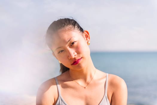 young contemplative asian woman at beach looking at camera, concept of beauty and purity, flare effect