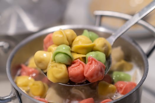In a pot, colorful dumplings are being boiled. Preparing lunch or dinner for children and family.