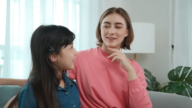 Happy mother sharing experience with daughter while sitting in living room. Caucasian mom and happy child talking and spend time together. Attractive girl listen parent story while smiling. Pedagogy.