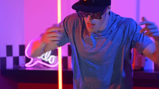 Skilled break dancer wearing fancy glasses with glowing effect while caucasian performer with casual shirt. Close up of skilled man moving to freestyle music and dancing in led light. Regalement.