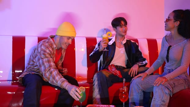 Multicultural friend clinking glass to celebrate their team work at home party with neon light. Professional diverse people with stylish fashion holding colorful juice and clink together. Regalement.