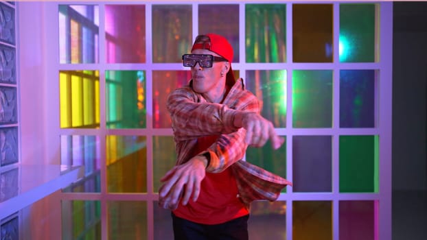 Funny break dancer moving freestyle step to hiphop while looking at camera. Crazy happy hipster dancing and performing street dancing while wear casual outfit and sunglasses in Led light. Regalement.