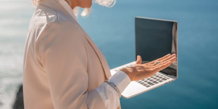 Freelance women sea working on the computer. Good looking middle aged woman typing on a laptop keyboard outdoors with a beautiful sea view. The concept of remote work