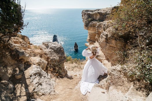 A woman in a white dress is walking on a rocky beach near the ocean. The scene is serene and peaceful, with the woman's dress flowing in the wind