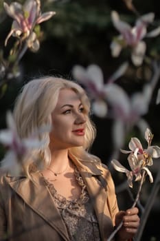 A woman is holding a magnolia flower in her hand and standing in front of a tree. Concept of serenity and beauty, as the woman is surrounded by nature and the flower adds a touch of color