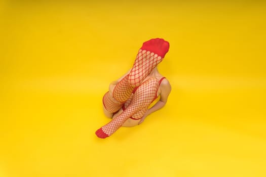 A woman with vibrant magenta fishnet stockings sits gracefully on a peachcolored rug, creating an artistic display against the yellow background