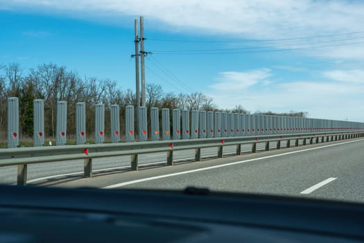 A road with a long line of metal posts with red hearts on them. The road is empty and the sky is clear