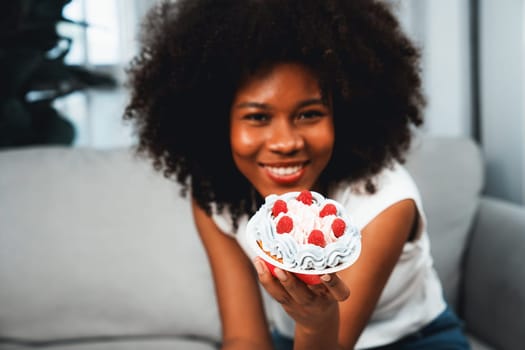 Beautiful young African blogger presenting cupcake with selective focus in concept special cuisine. Content creating of social media online with favorite sweets bakery dish. Tastemaker.