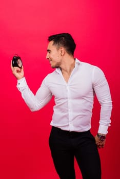 Emotional young man holding clock on a red background. Being late concept