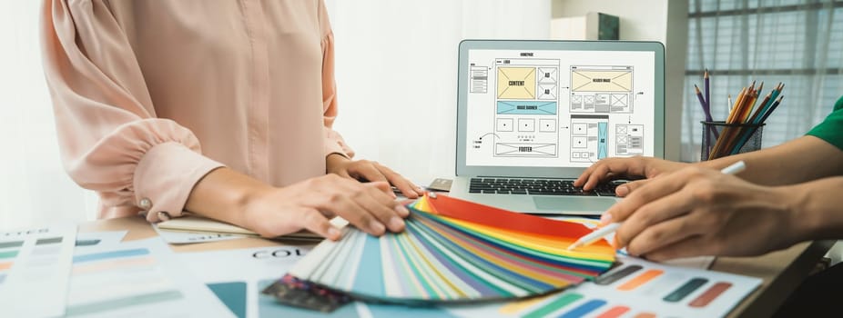 Cropped image of interior designer chooses color from color swatches while laptop displayed website wireframe designs for mobiles app and website. Creative design and business concept. Variegated.