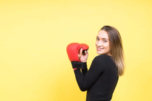 Portrait of young woman in a casual clothes and hands in boxing gloves against yellow background
