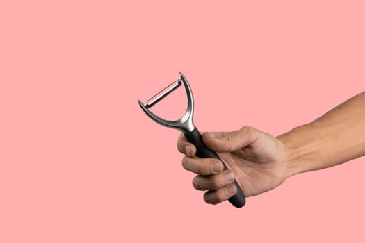 Black male hand holding a potato peeler isolated on pink background. High quality photo